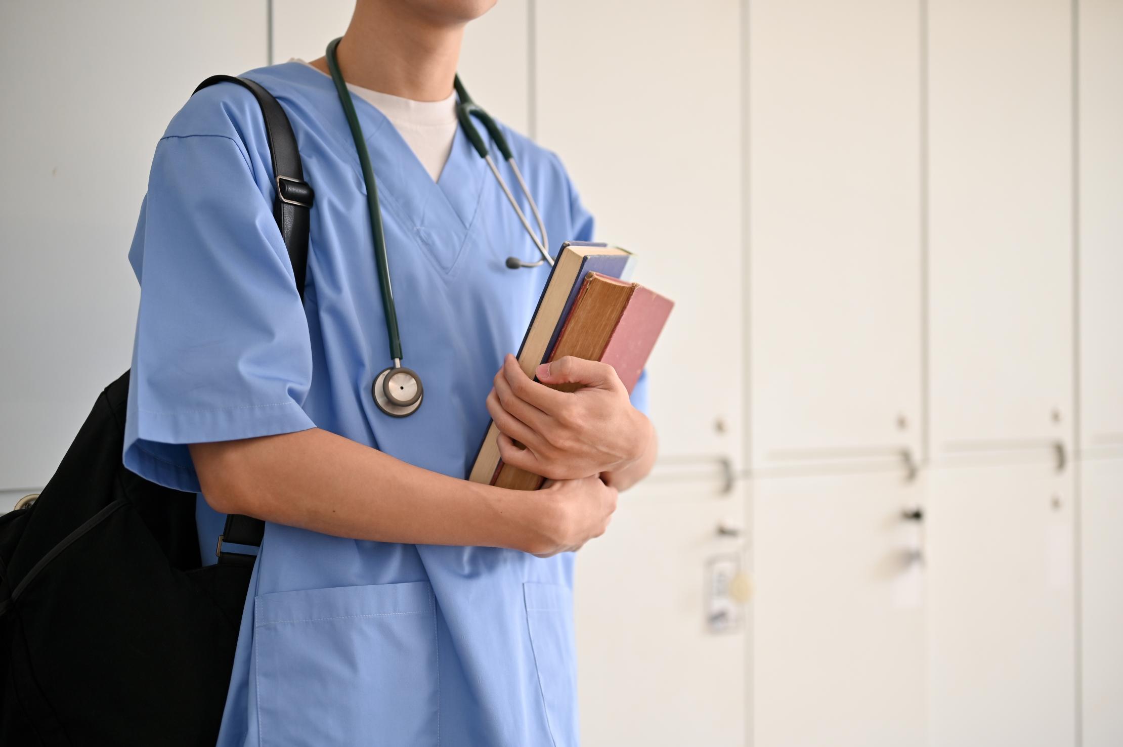 Person trägt Arztkittel und hält Bücher in der Hand